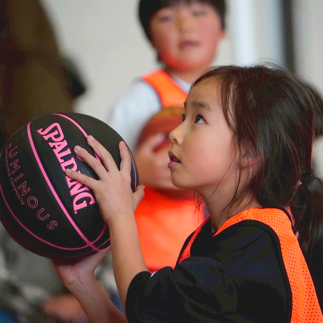 ボールを両手で持ち、ゴールの方を見上げる子ども